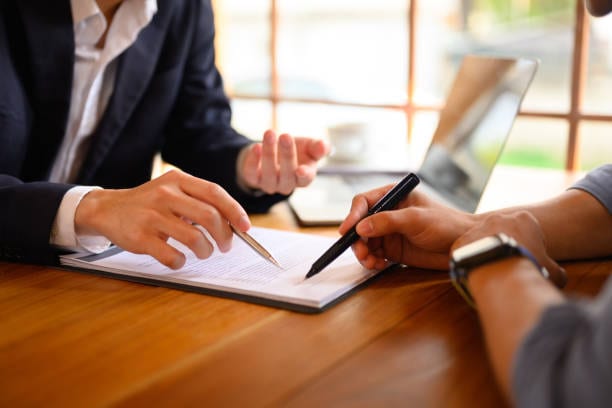 Dos personas revisando y firmando un documento sobre una mesa de reuniones